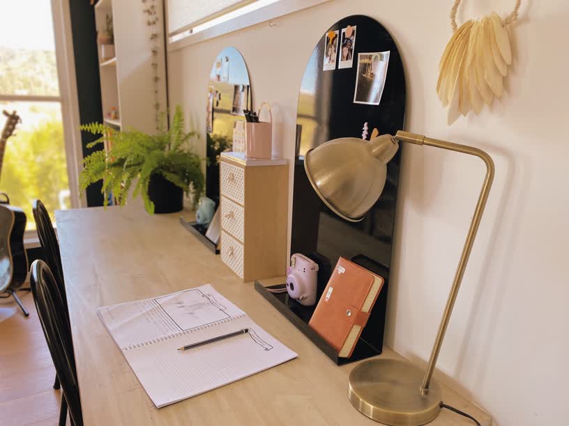Wooden desk with open notebook, pencil, and brass lamp. Black and white shelves hold plants and decor. Bright window in background. Cozy mood. Tiffany Boyd, Freely Homeschool Planner Founder sharing her Homeschool and favourite resources
